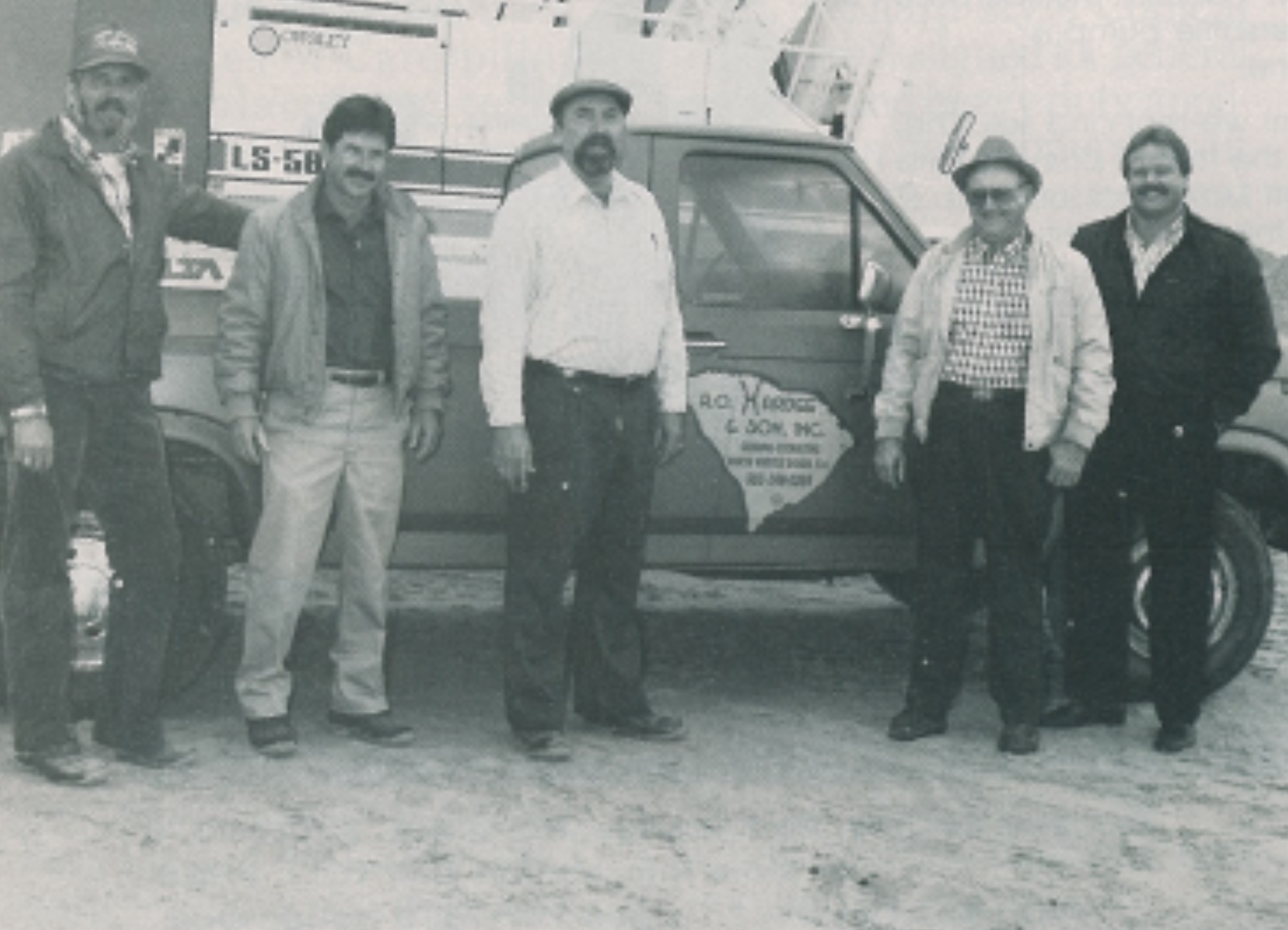 Five men pose by a pickup truck with company logo.